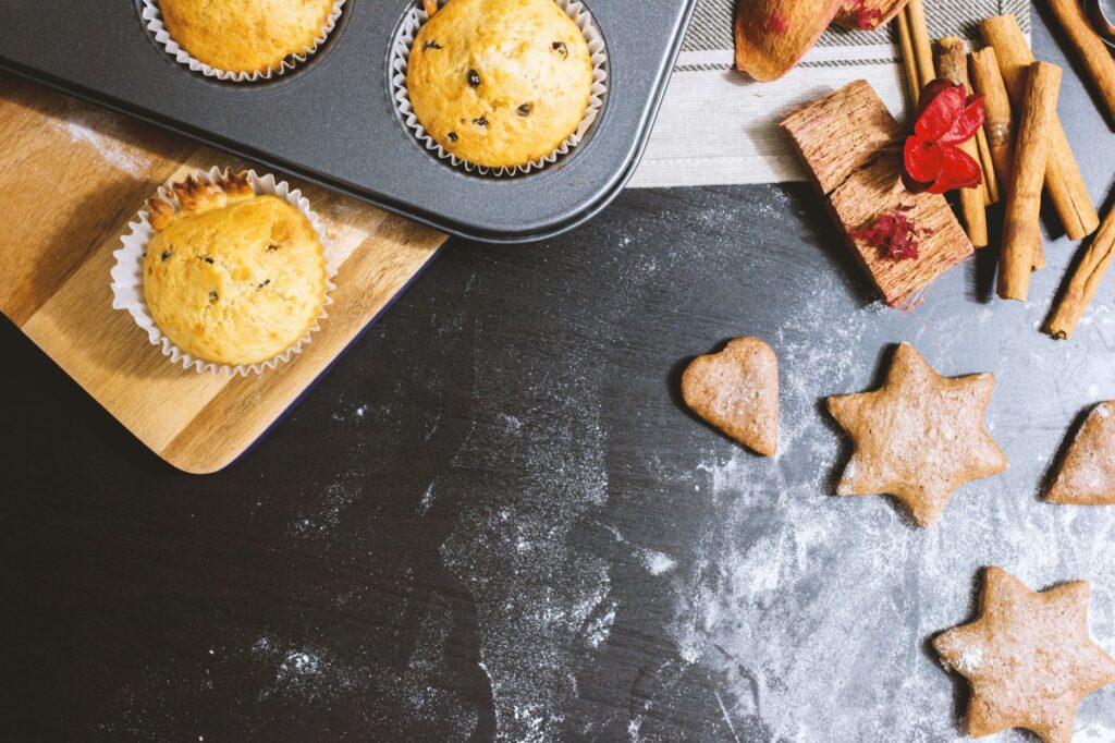 Une délicieuse disposition de muffins et de biscuits avec de la cannelle et de la farine sur un plan de travail noir.