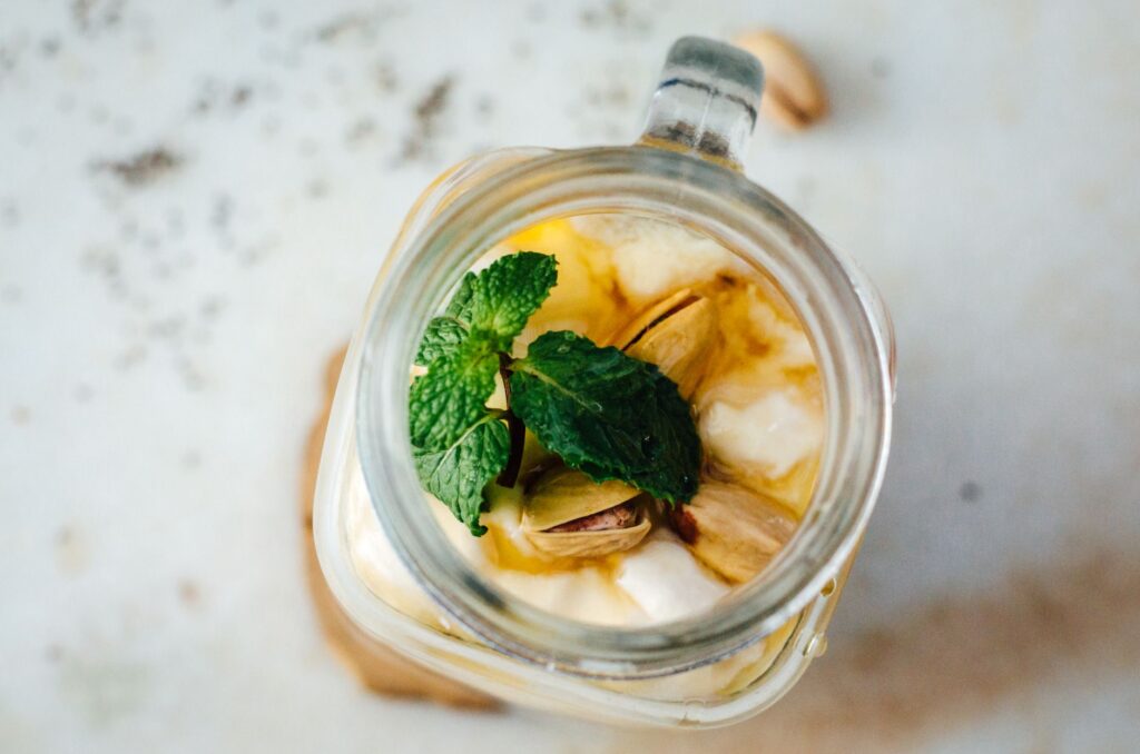 Vue en gros plan d'un pot de yaourt crémeux, de pistaches et de feuilles de menthe, parfait pour une collation douce et saine.
