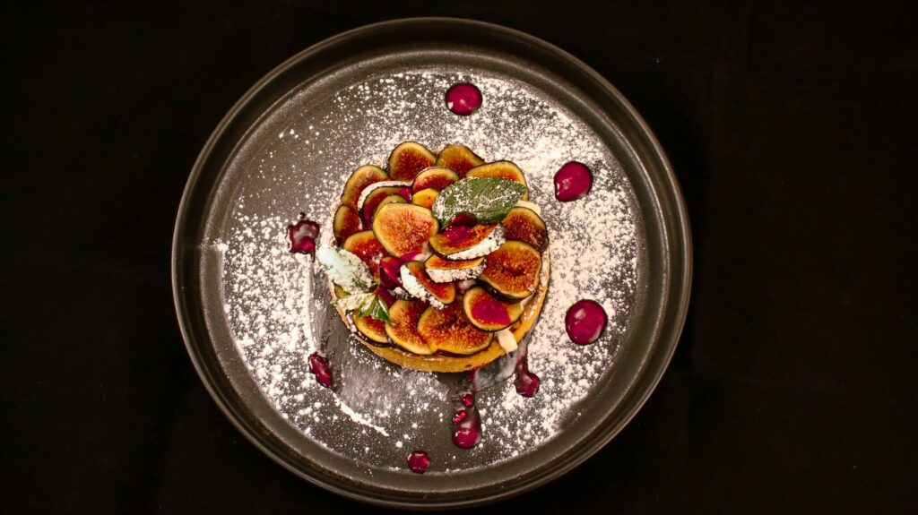 Délicieuse tarte aux figues présentée avec du sucre glace et de la sauce sur une assiette sombre.
