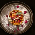Délicieuse tarte aux figues présentée avec du sucre glace et de la sauce sur une assiette sombre.