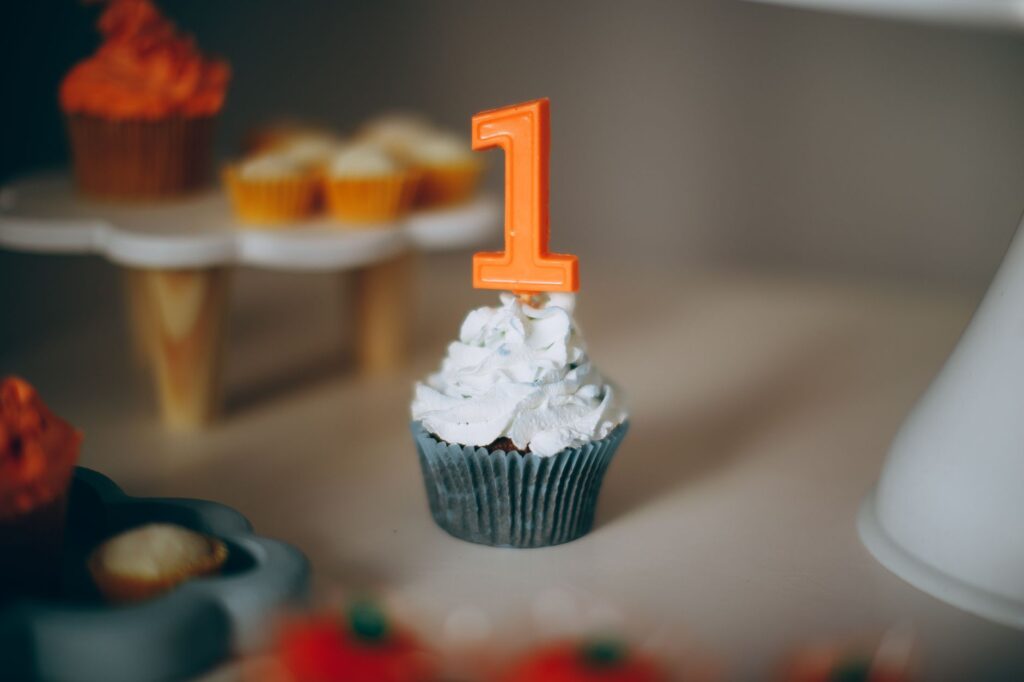 Un cupcake bleu avec un glaçage blanc et une bougie orange en forme de 1, idéal pour fêter un premier anniversaire.
