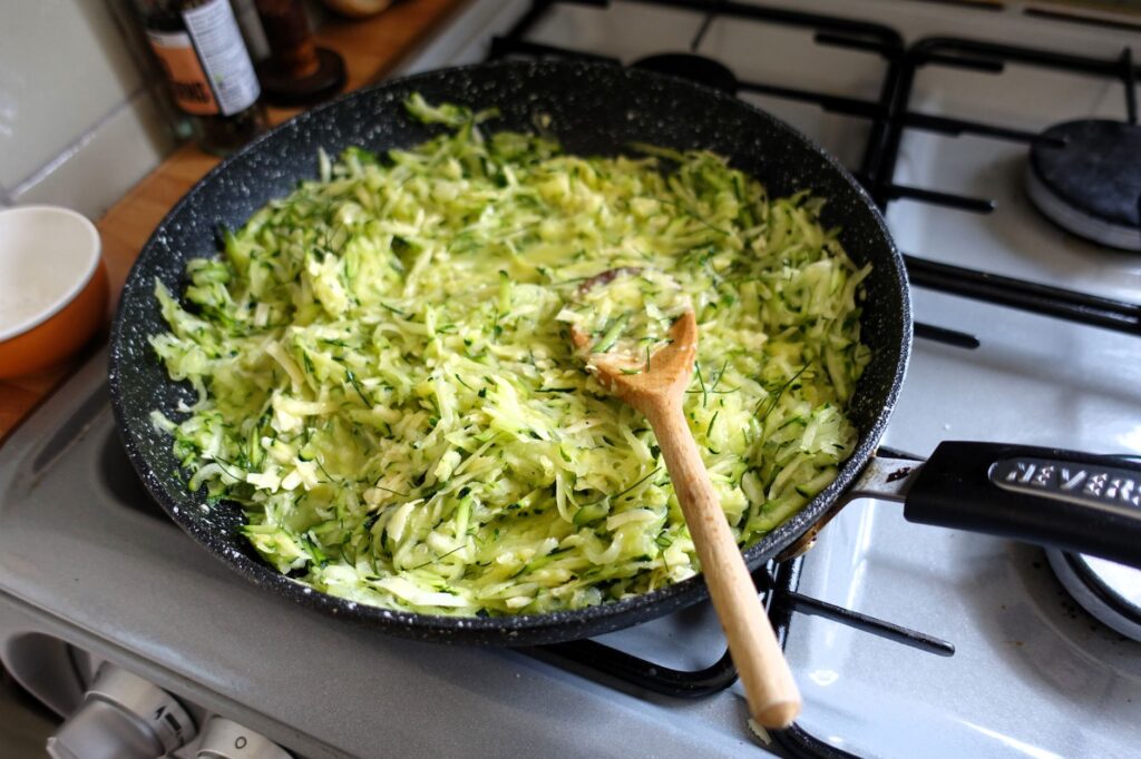 Des courgettes fraîchement râpées en train de cuire dans une poêle sur une cuisinière moderne.