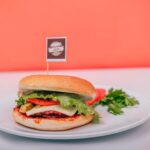Un burger végétarien avec de la laitue, du fromage et des tomates sur une assiette contre un fond vibrant.