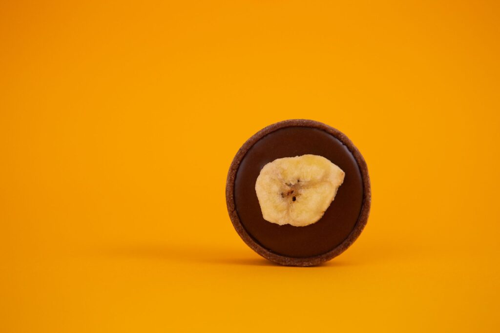 Une photo minimaliste d'une tarte au chocolat garnie d'une tranche de banane sur un fond jaune audacieux.