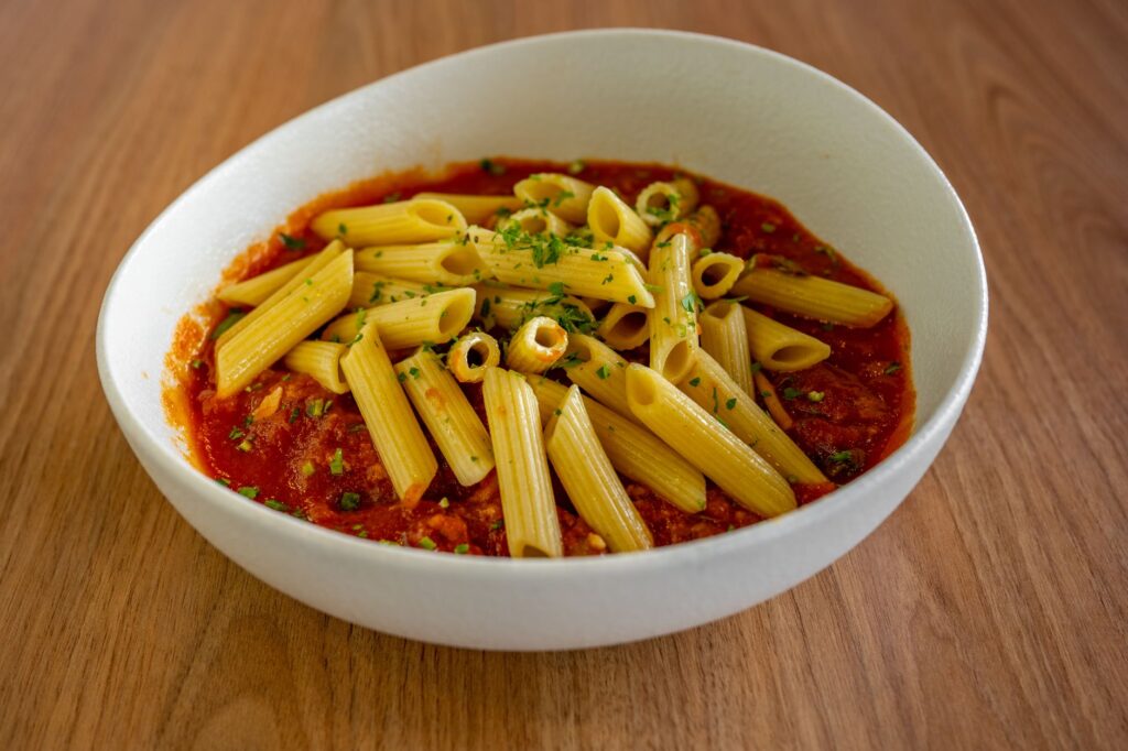 Pâtes penne servies dans une sauce tomate savoureuse, garnie d'herbes, dans un bol blanc sur une table en bois.