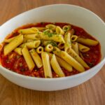 Pâtes penne servies dans une sauce tomate savoureuse, garnie d'herbes, dans un bol blanc sur une table en bois.