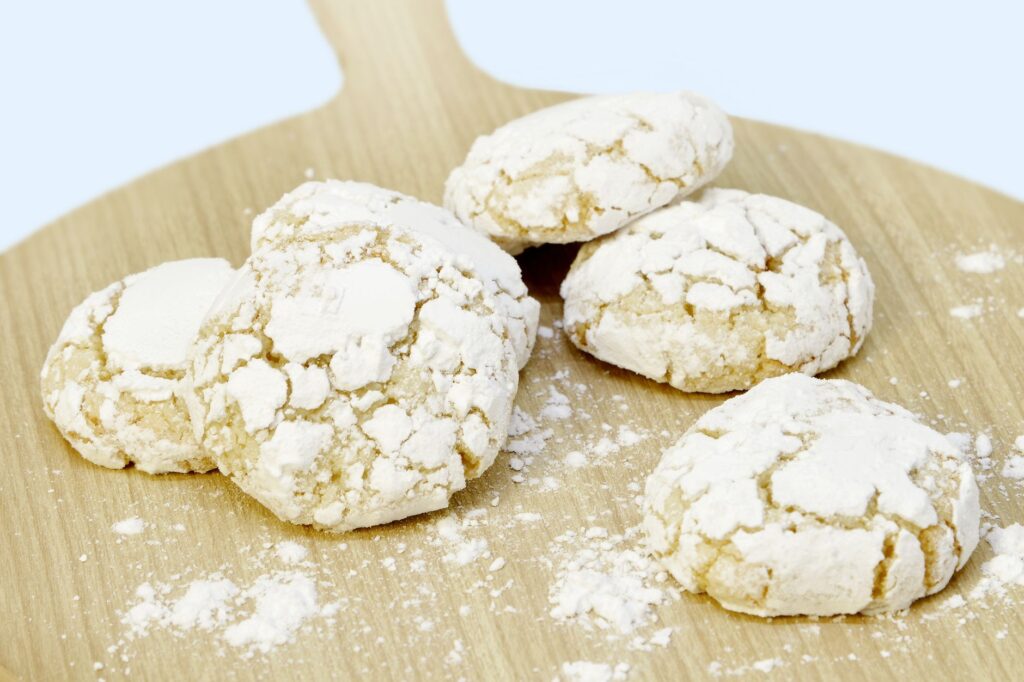 Délicieux biscuits marocains aux amandes saupoudrés de sucre glace, présentés sur une planche en bois.