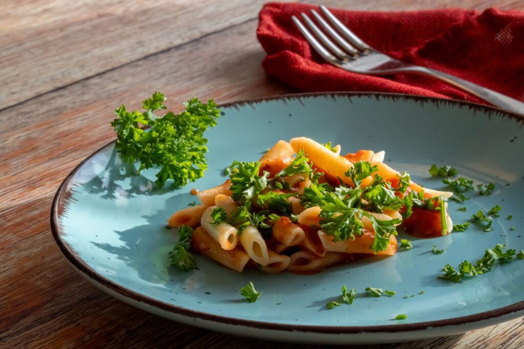 Délicieuses pâtes penne garnies de persil frais et de sauce tomate sur une assiette bleue.
