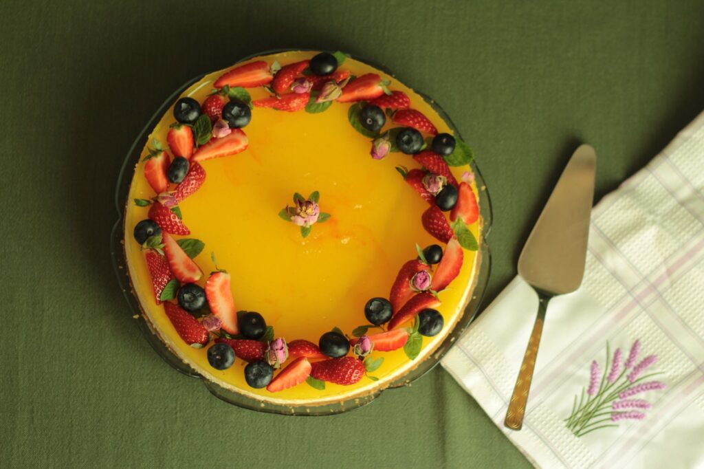 Gâteau au fromage vibrant garni de fruits avec des fraises et des myrtilles sur une nappe verte.