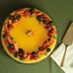 Gâteau au fromage vibrant garni de fruits avec des fraises et des myrtilles sur une nappe verte.