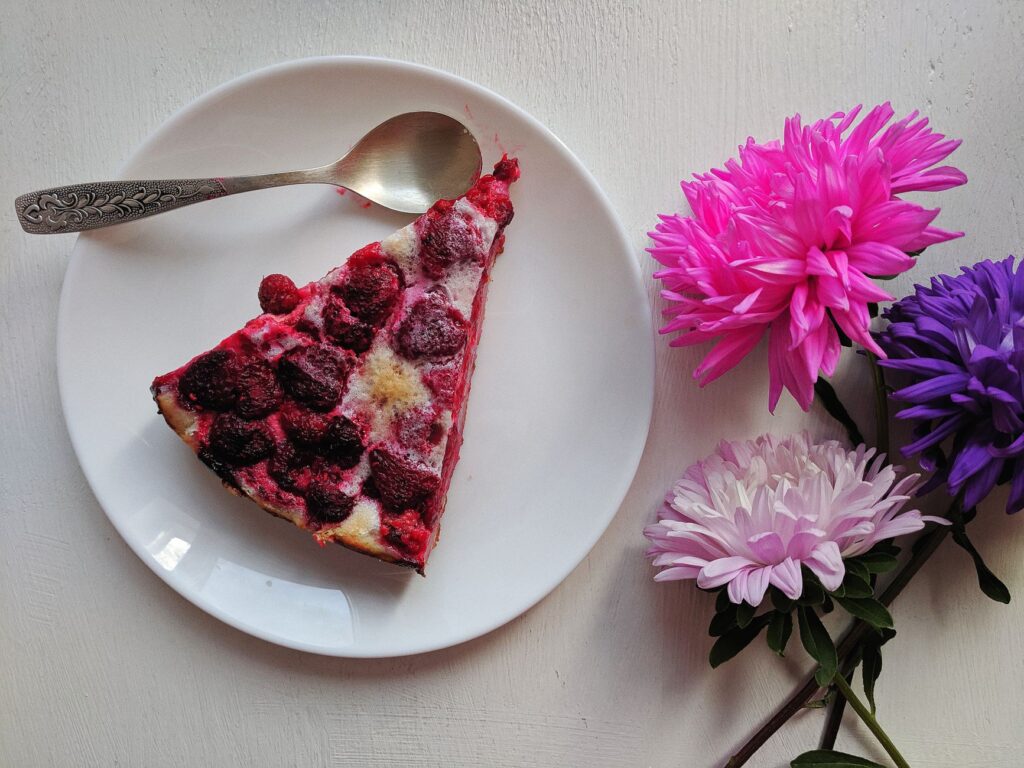 Une part de pâtisserie à la framboise sur une assiette à côté de fleurs colorées, parfaite pour les amateurs de desserts.