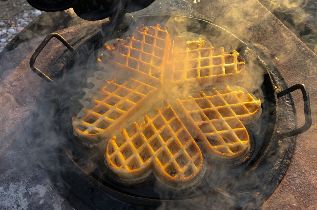 De délicieuses gaufres dorées cuisent dans une poêle en fonte en forme de cœur avec de la vapeur.