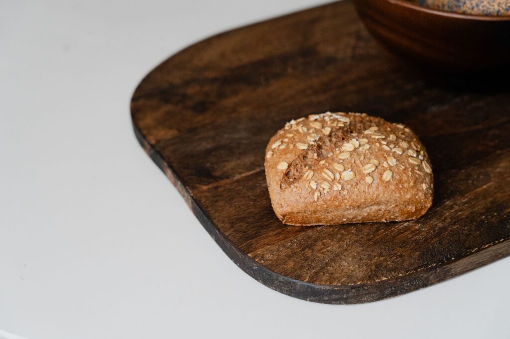 Une petite boule de pain complet fraîchement cuite avec des flocons d'avoine reposant sur une planche en bois rustique.