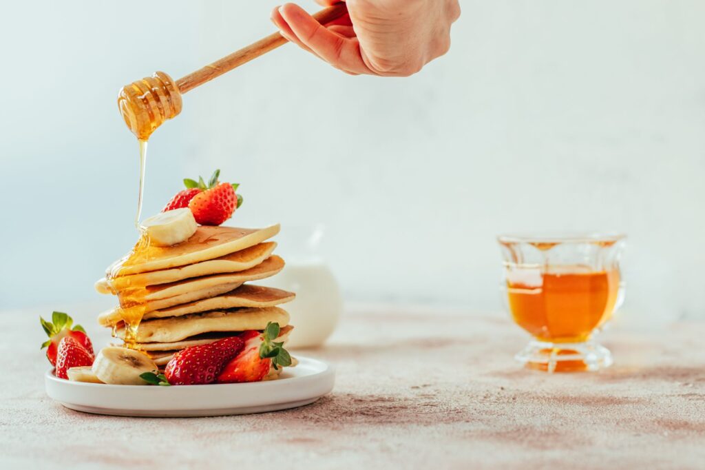Pile de crêpes avec miel, banane et fraises, créant une scène de brunch parfaite.