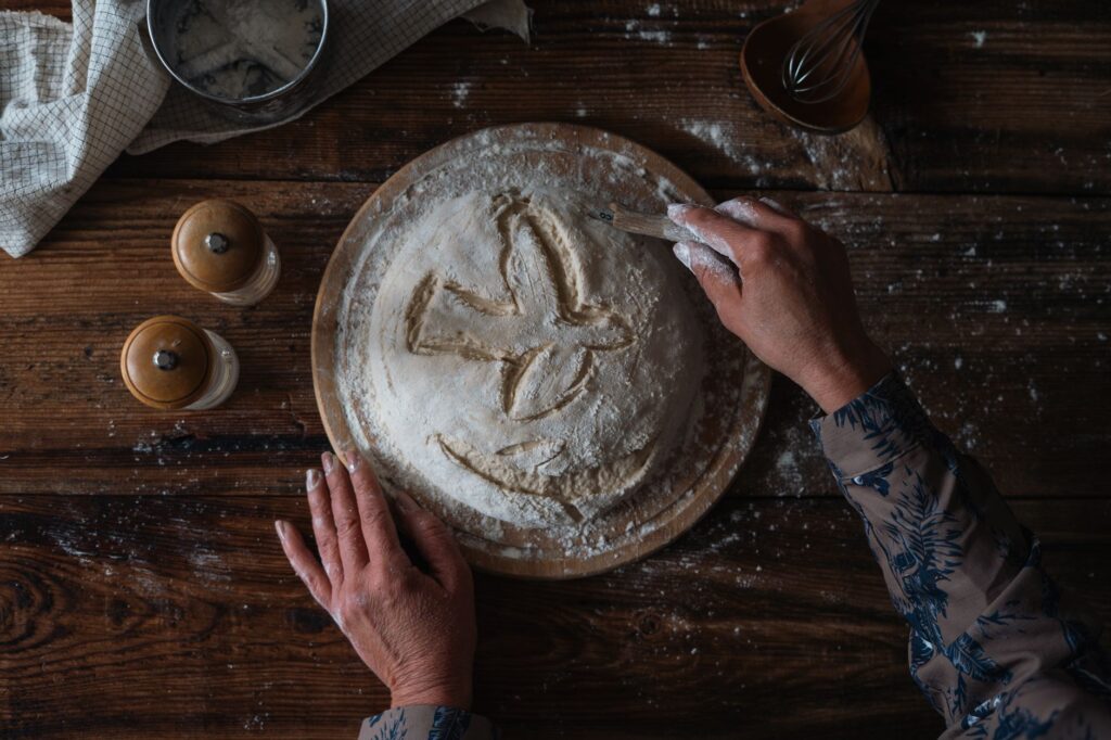Une personne sculpte des motifs dans de la pâte à pain sur une table en bois rustique, mettant en valeur la pâtisserie traditionnelle.