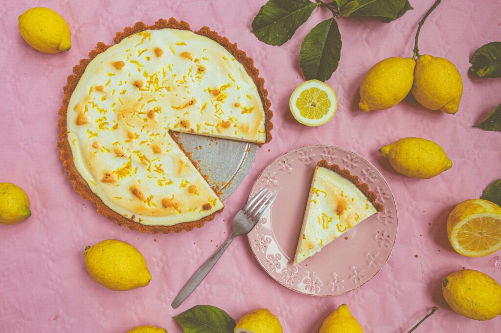 Vue de dessus d'une tarte au citron avec des citrons frais sur fond rose, parfaite pour l'inspiration dessert.