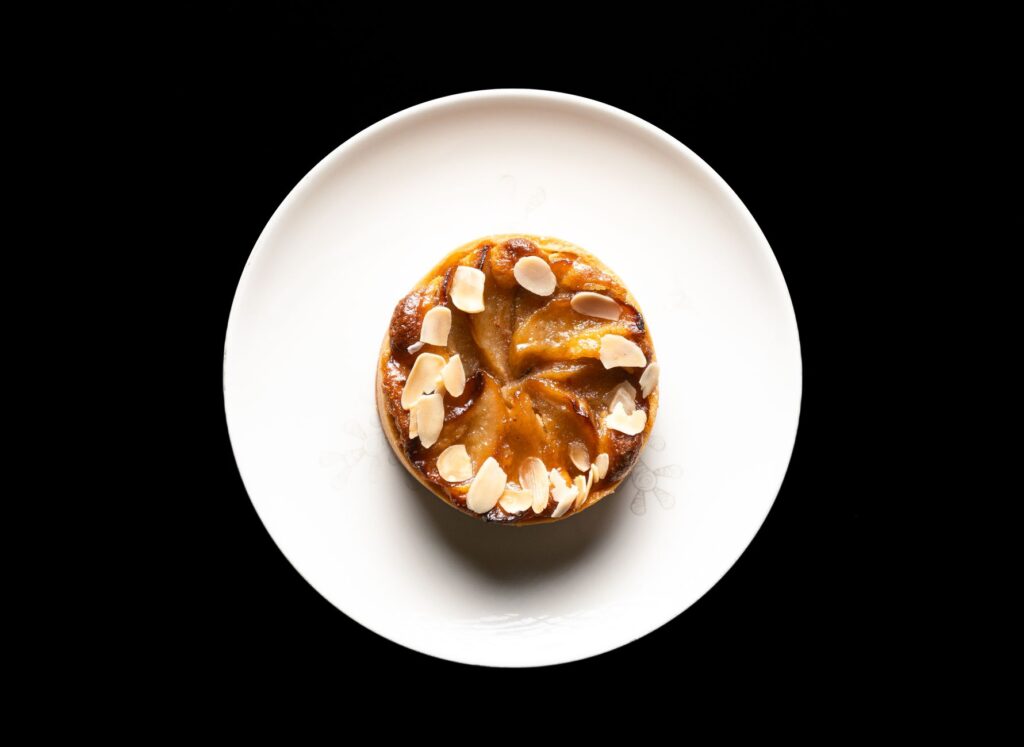 Une délicieuse tarte aux amandes avec des amandes effilées est posée élégamment sur une assiette blanche sur un fond noir.