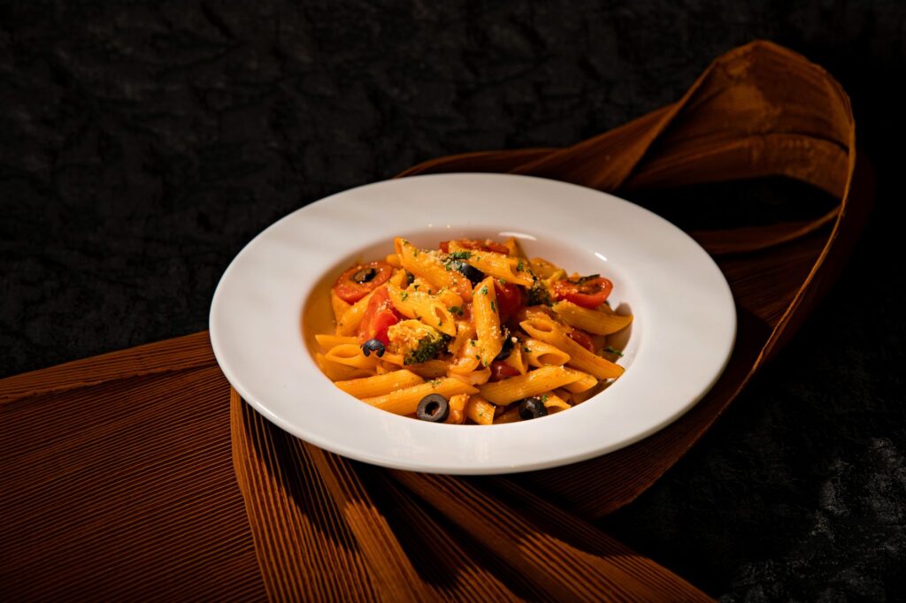 Pâtes penne vibrantes aux légumes dans une assiette blanche, sur fond sombre.