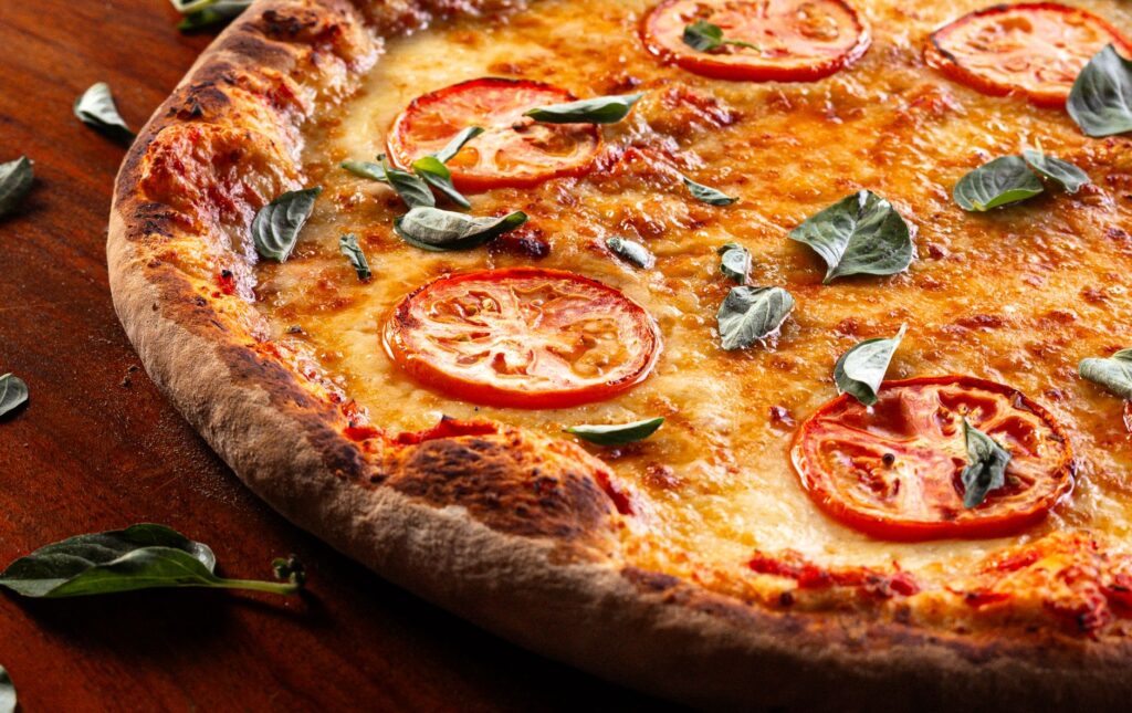 Vue rapprochée d'une pizza Margherita garnie de tranches de tomates fraîches et de feuilles de basilic.