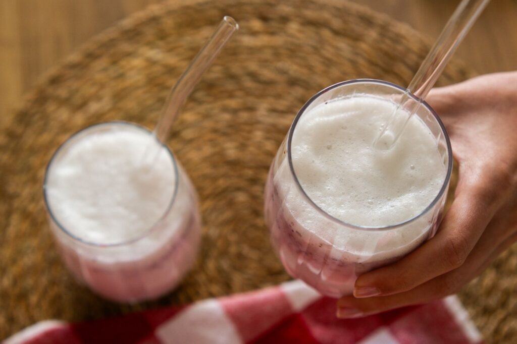 Deux verres de lait glacé aux baies avec de la mousse, servis avec des pailles en verre sur un tapis tissé.