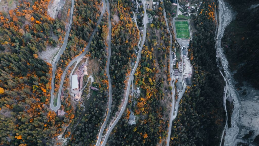 Superbe vue aérienne de routes de montagne sinueuses entourées de feuillage d'automne et d'un terrain de football à Anniviers, en Suisse.