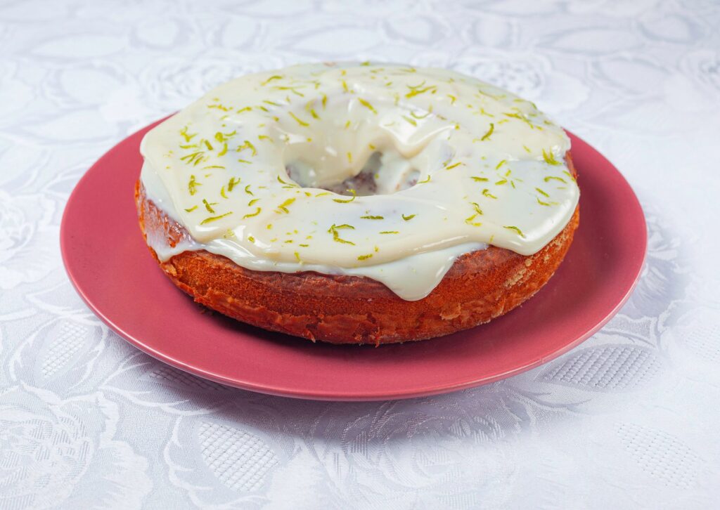 Gros plan d'un gâteau Bundt glacé au citron vert sur une assiette rose avec une nappe complexe.