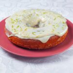 Gros plan d'un gâteau Bundt glacé au citron vert sur une assiette rose avec une nappe complexe.