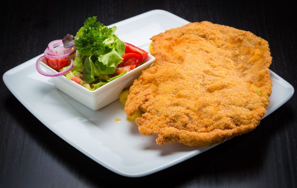Escalope panée dorée et croustillante servie avec une salade de légumes frais, présentée sur une assiette carrée.