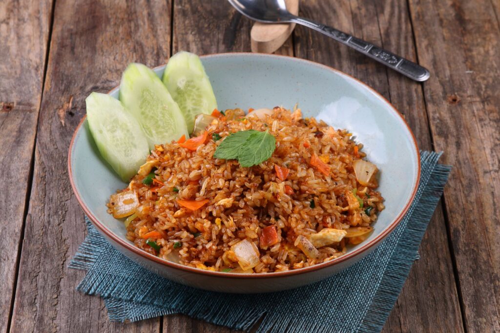 Un bol de riz frit aux légumes garni de tranches de concombre frais, servi sur une table rustique en bois.