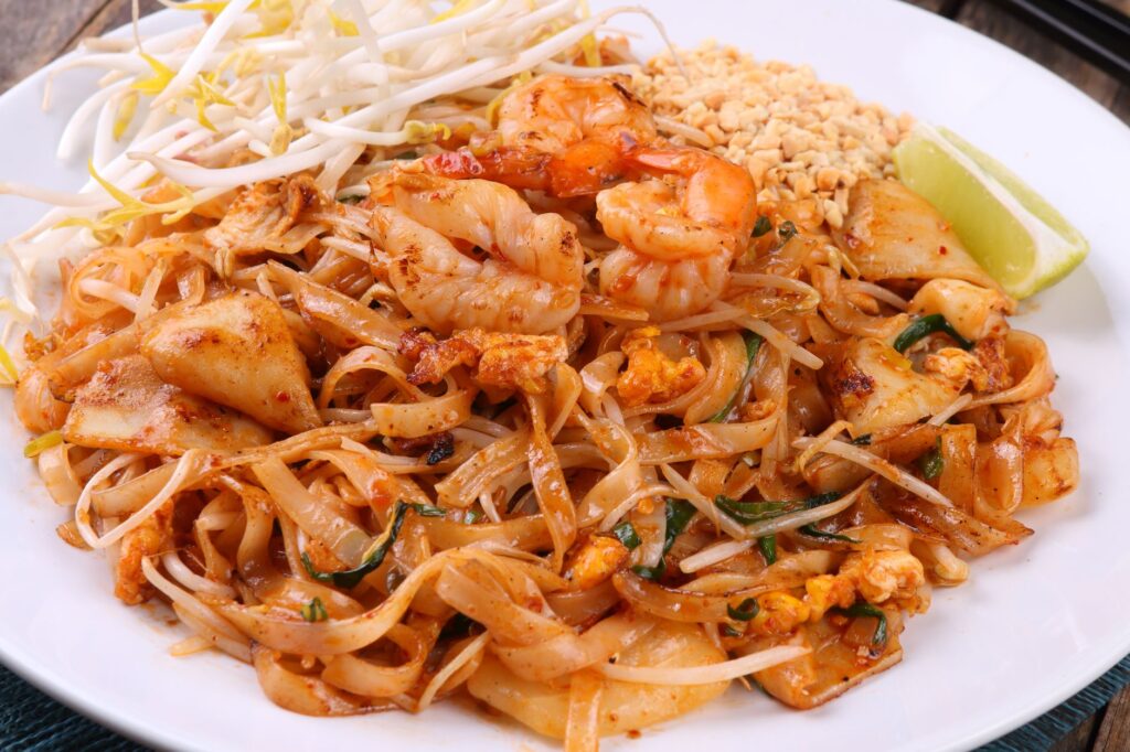 Assiette colorée de pad thaï aux crevettes, citron vert, cacahuètes et germes de soja.