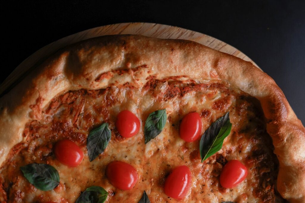 Gros plan sur une pizza Margherita garnie de tomates cerises et de basilic, servie sur une planche en bois.