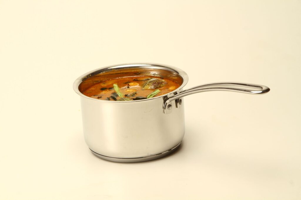 Gros plan sur un sambar du sud de l'Inde servi dans un pot en acier inoxydable sur fond blanc.