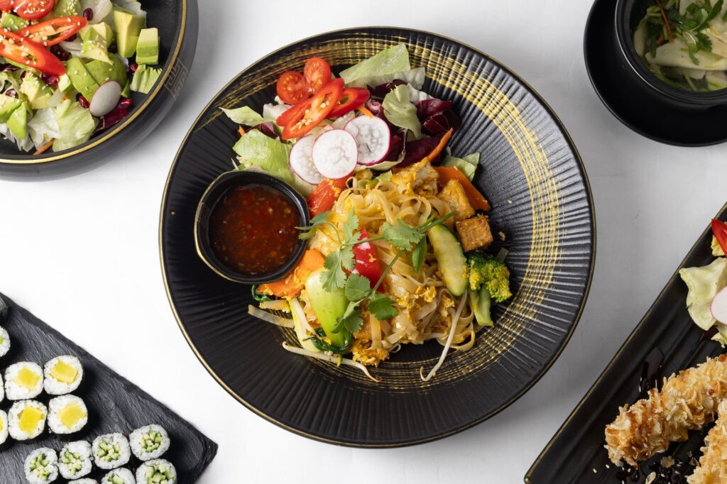 Plat de nouilles asiatiques coloré avec légumes frais et sushis, présenté à plat.