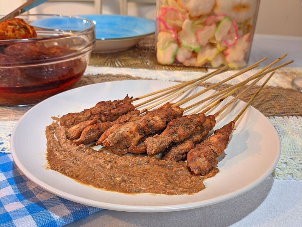 Brochettes de poulet satay indonésiennes servies avec une sauce aux arachides et des accompagnements traditionnels.