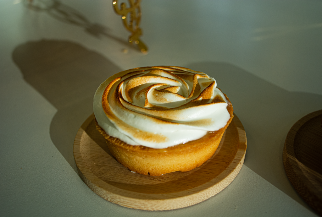 Tarte au citron meringuée dorée, nappée de crème onctueuse, présentée sur un plateau en bois à la lumière naturelle.