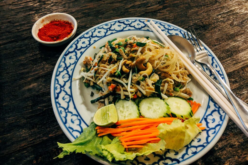 Une salade de nouilles asiatiques joliment présentée avec des légumes frais et un accompagnement de poudre de piment.