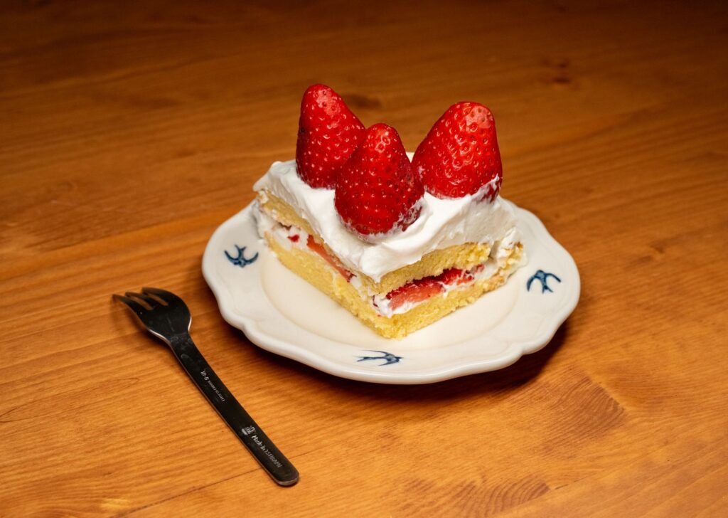 Une part tentante de gâteau aux fraises surmontée de fraises fraîches sur une assiette décorative.