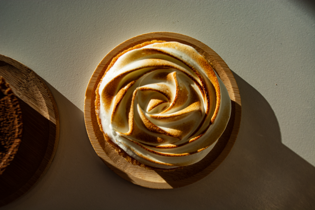 Délicieuse tarte au citron meringuée à la croûte dorée, présentée sur une assiette en bois et baignée d'une lumière chaude.