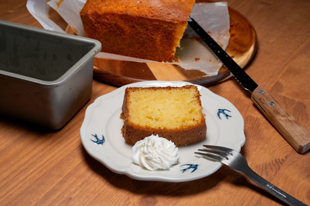 Une tranche de gâteau maison avec une cuillerée de crème chantilly, servie sur une assiette décorative.