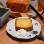 Une tranche de gâteau maison avec une cuillerée de crème chantilly, servie sur une assiette décorative.