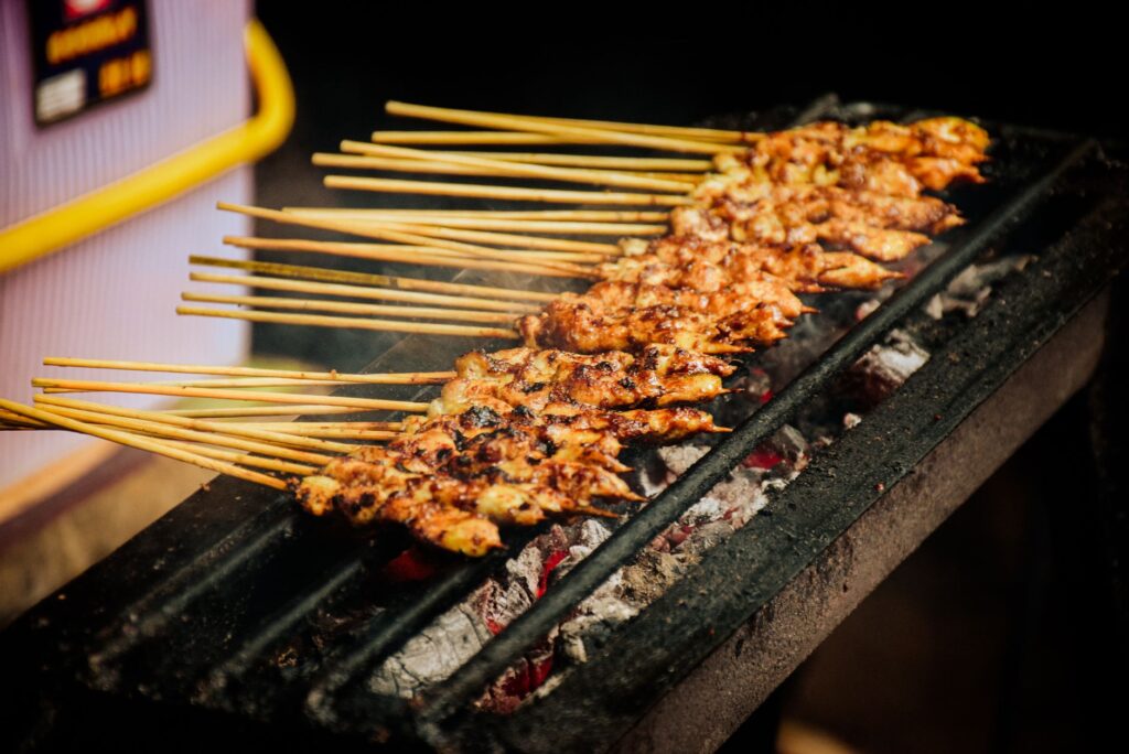 Gros plan sur des brochettes de satay de poulet grillant sur charbon de bois, mettant en valeur cette délicatesse de la street food.