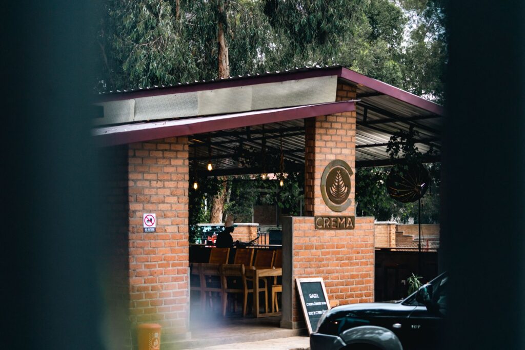Café extérieur avec des murs en briques, présentant une enseigne Crema, des sièges et de la verdure.