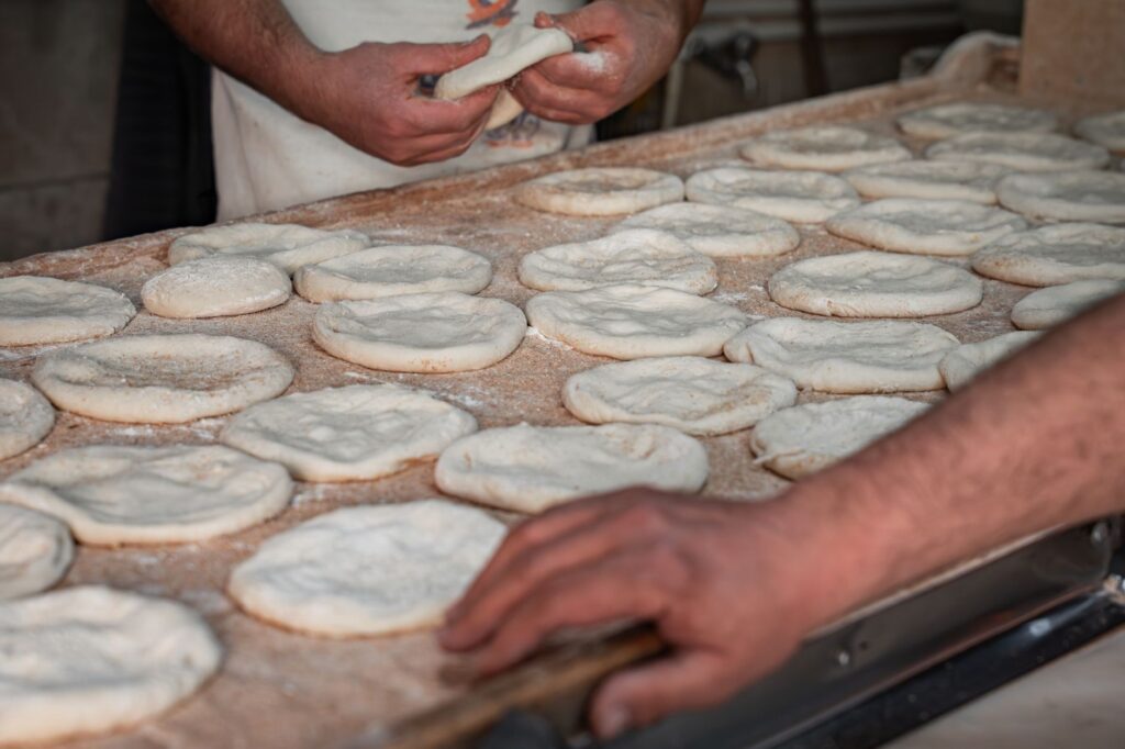 Des boulangers artisanaux façonnent de la pâte à pain pita fraîche à la main dans un cadre de boulangerie traditionnel.