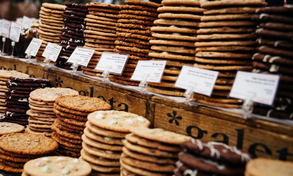 Assortiment de biscuits élégamment empilés et étiquetés dans un stand de marché animé.