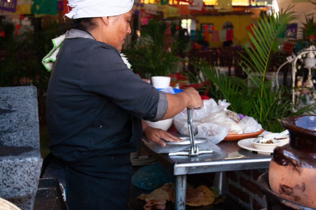 Scène authentique d'une femme préparant des tortillas à la main en extérieur, mettant en valeur la cuisine mexicaine traditionnelle.