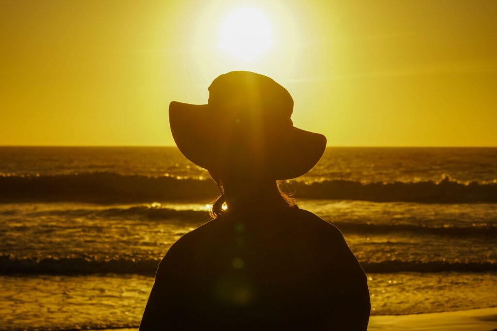 Une silhouette portant un chapeau se détache sur un coucher de soleil flamboyant au-dessus de l'océan, créant une scène sereine et contemplative.