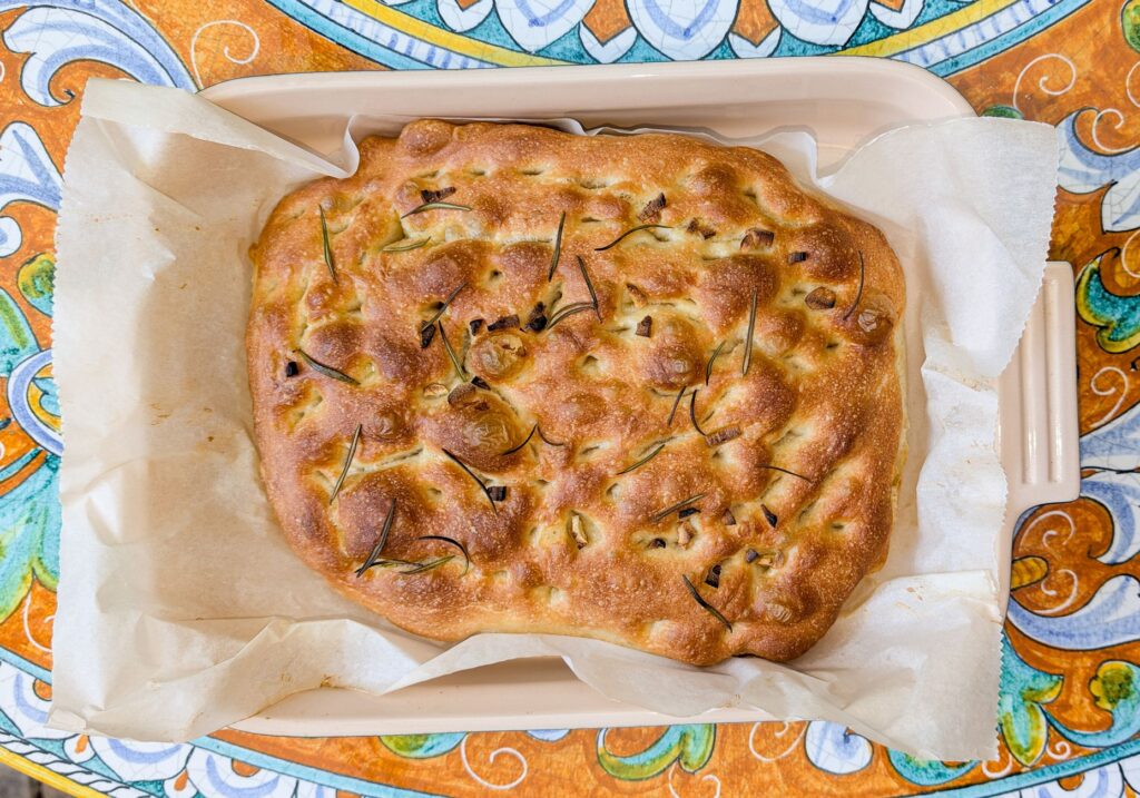 Focaccia dorée garnie de romarin et d'oignon, servie sur du papier sulfurisé.
