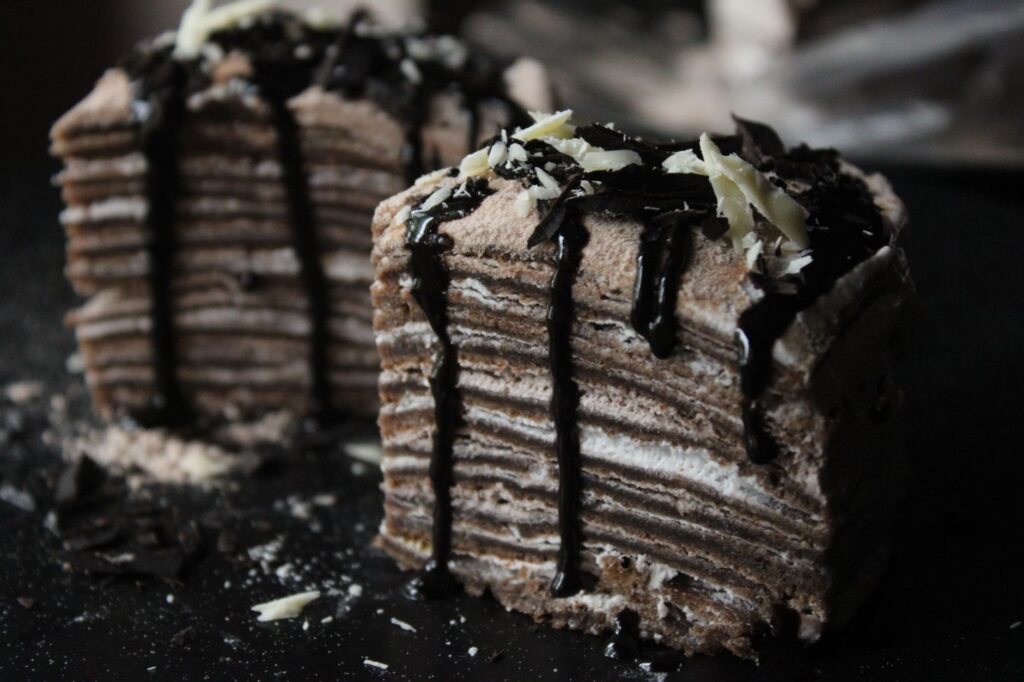 Gâteau de crêpes à étages nappé d'un riche filet de chocolat et garni de copeaux de chocolat.