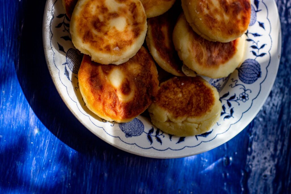 Gros plan sur des crêpes au fromage dorées, servies sur une assiette décorative sur fond bleu.