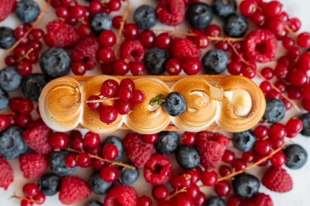 Dessert recouvert de meringue, entouré de groseilles rouges, de framboises et de myrtilles éclatantes.